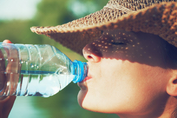 Woman with hat and sunlight on her face while drinking water