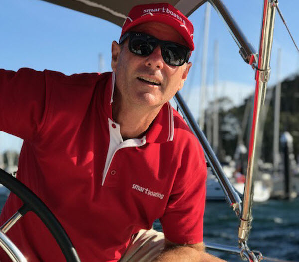 Man wearing a red shirt and sun glasses while stirring the wheel of a boat